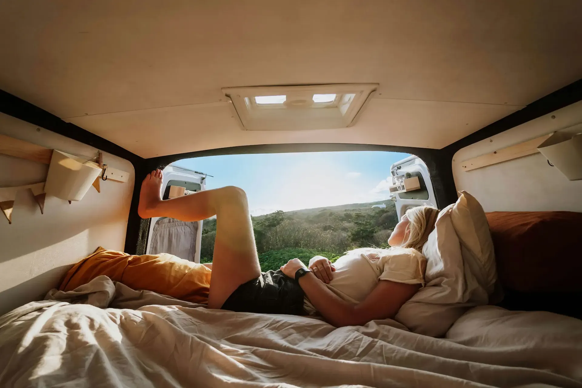 "Persona descansando en una cama dentro de una furgoneta camper con vistas a la naturaleza